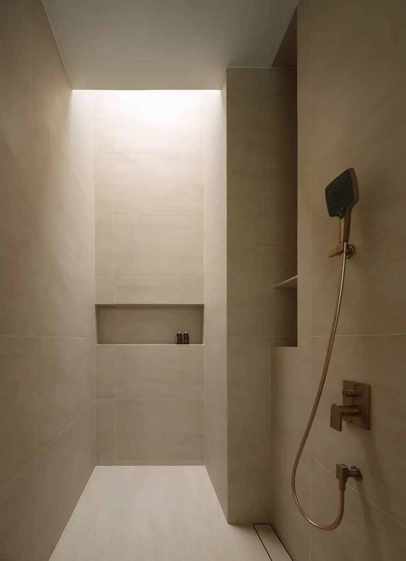 Shower enclosure with recessed niche lit by concealed ceiling light and warm stone tile walls