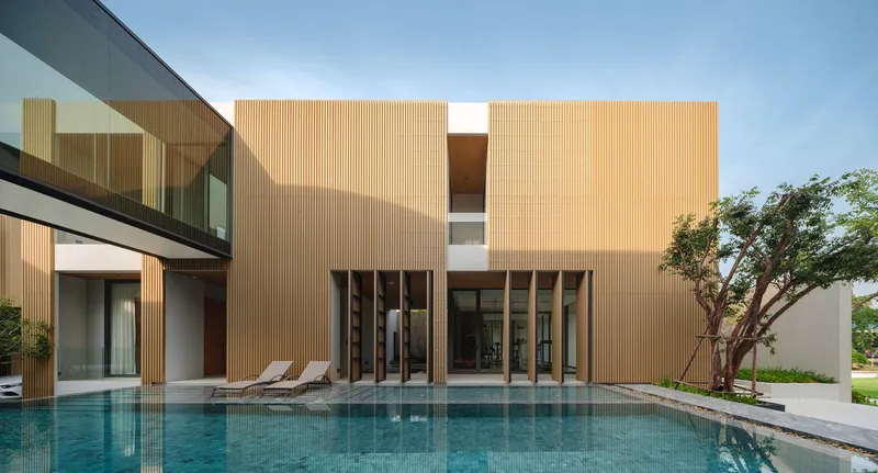 Rear facade with vertical timber cladding and recessed openings overlooking a swimming pool and lounge chairs