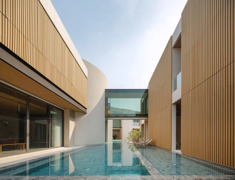 Courtyard pool between vertical timber-clad facades and a glazed bridge under open sky