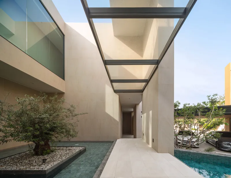 Covered walkway with steel and glass canopy connecting courtyard volumes with planted olive tree and pool