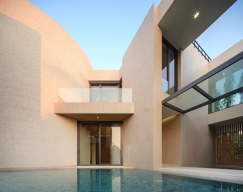 Courtyard pool at dusk with cantilevered balcony and floor-to-ceiling glazed entrance below