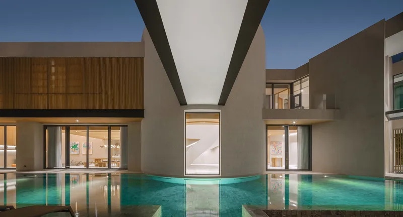Illuminated courtyard pool at twilight framed by volumes with timber cladding and glass walls