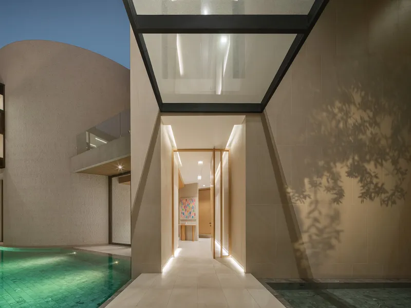 Glass-roofed passage at dusk with tree shadows cast on limestone wall and pool edge