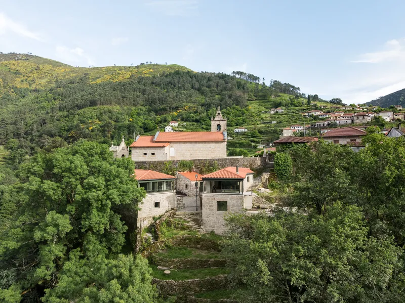Cluster of stone houses with terracotta roofs and church bell tower set within terraced green hillsides