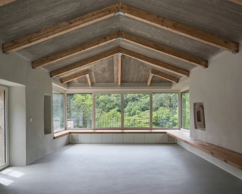 Interior room with exposed timber truss ceiling, continuous window bench and polished concrete floor facing the landscape