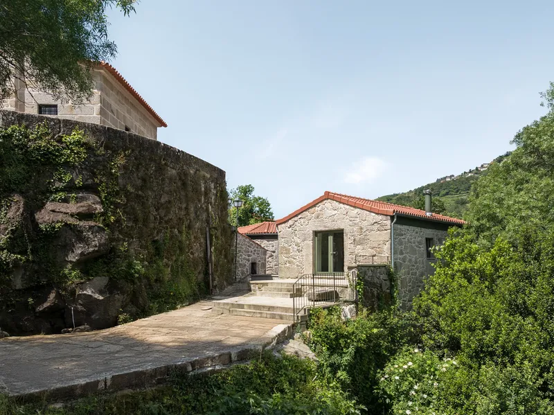 Stone paved terrace connecting volumes with terracotta roofs and a stone staircase among trees