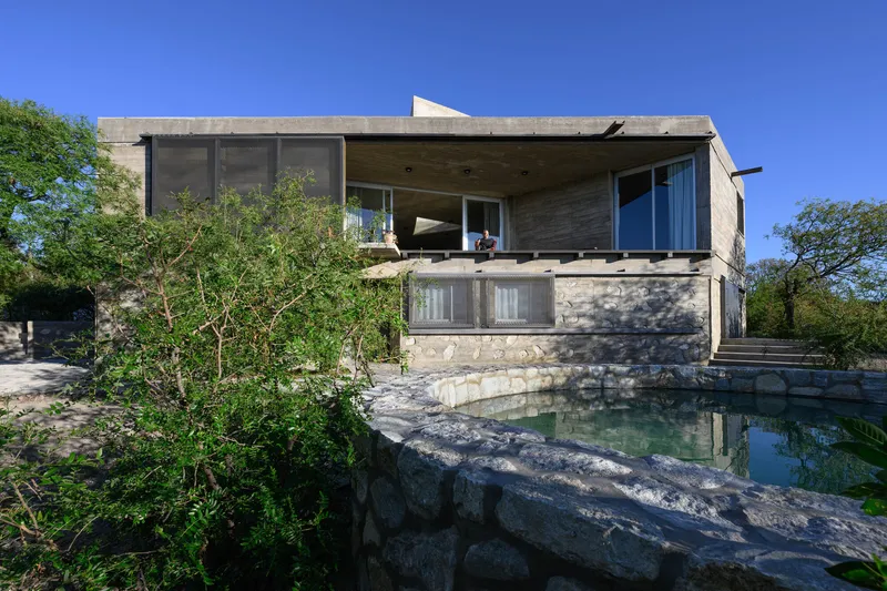 Two-story concrete volume with screened upper terrace and reflecting pool edged by natural stone