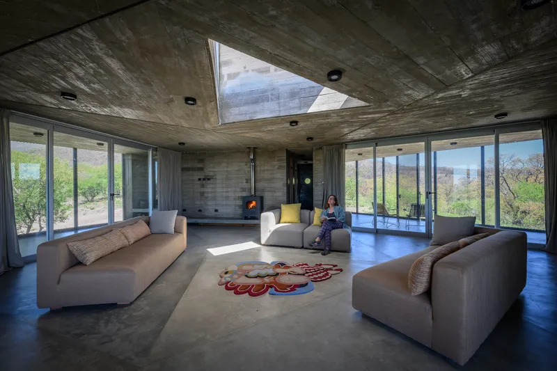 Open living room with board-formed concrete ceiling, triangular skylight, and a seated figure reading