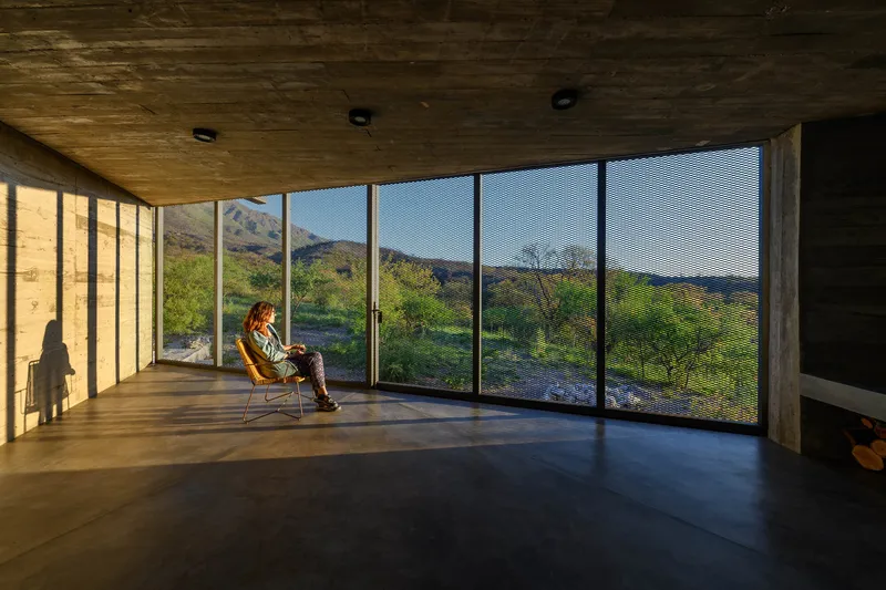 Interior room with floor-to-ceiling glazing overlooking mountainous landscape, timber ceiling overhead with a seated figure