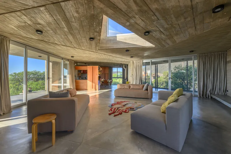 Living room with boardform concrete ceiling and triangular skylight surrounded by floor-to-ceiling glazing