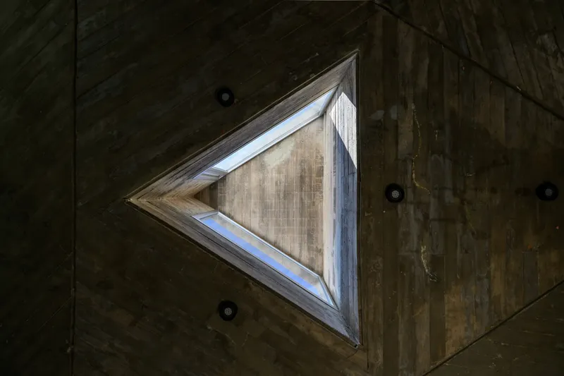 Upward view of triangular skylight framed by boardform concrete ceiling with recessed lighting fixtures