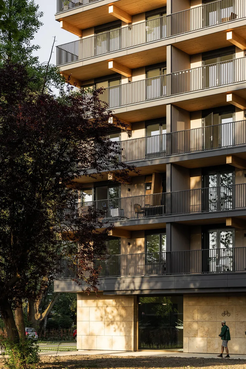 Ground floor entrance with light stone cladding framed by vertical slat balconies and foliage shadows