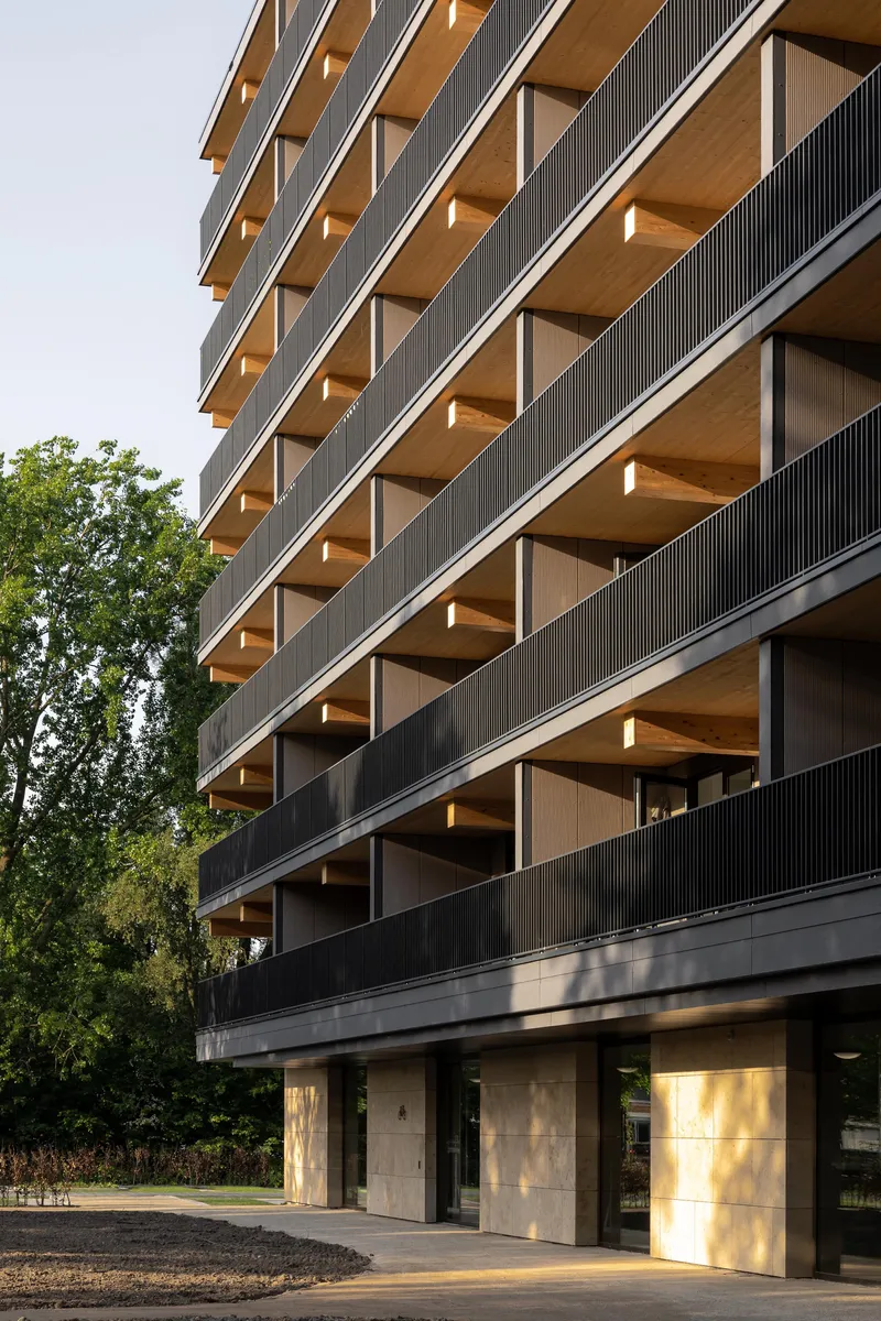 Stacked timber-lined balconies with vertical metal screening and concrete columns at ground level