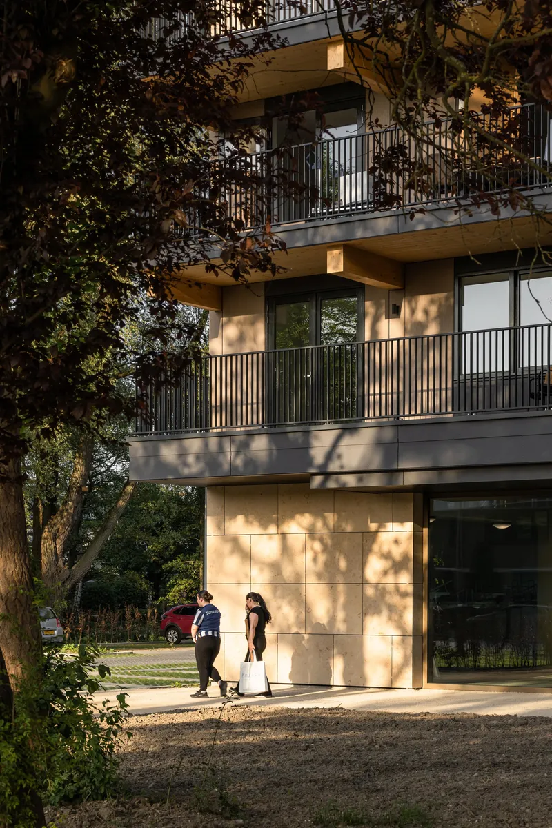 Timber-clad balconies casting dappled shadows with two pedestrians near the entrance at sunset