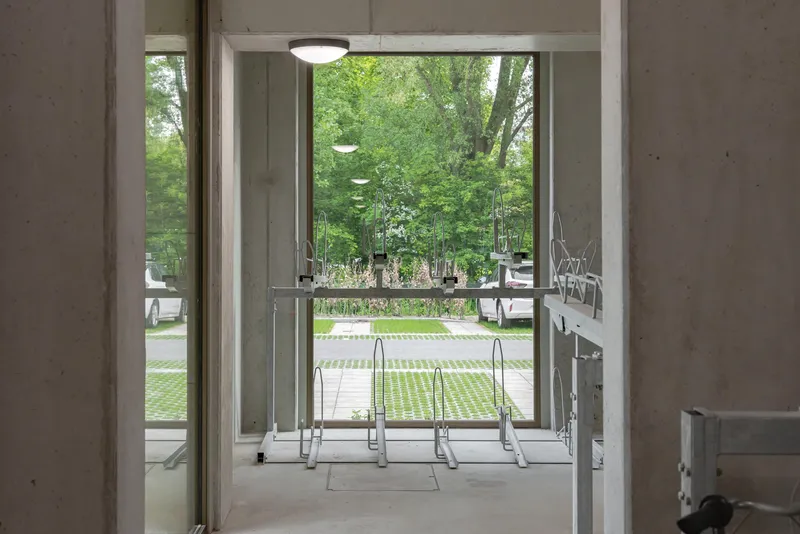 Glass table and chairs in concrete interior opening to landscaped courtyard with planted beds