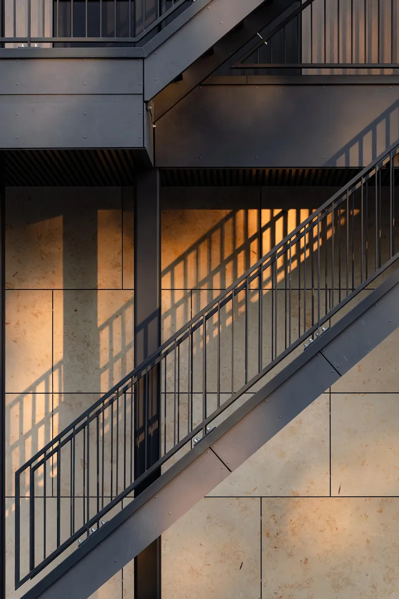 Exterior staircase with metal railings casting shadow patterns across concrete and plaster walls at sunset