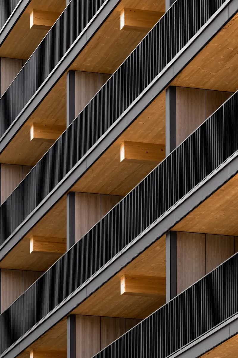Facade detail showing diagonal balconies with dark corrugated screens and timber soffits in repeating rhythm