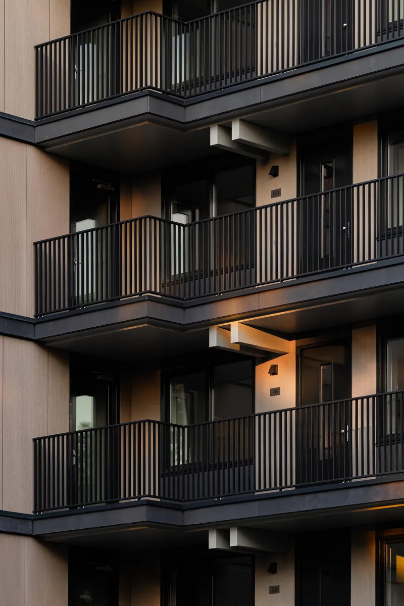 Stacked balconies with vertical metal railings and recessed openings illuminated at twilight