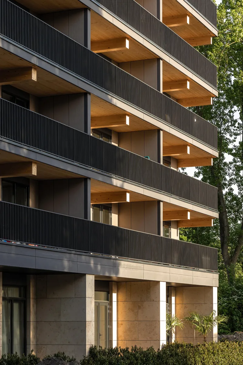 Multi-story facade showing timber balcony soffits and concrete base with planted beds at ground level