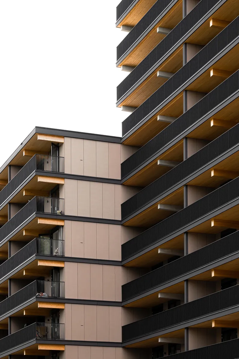 Close-up of stacked balconies with timber soffits and dark metal railings against an overcast sky