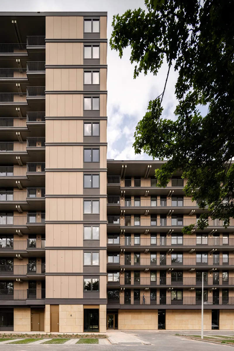 Street view of two residential towers with vertical panel cladding framed by deciduous trees