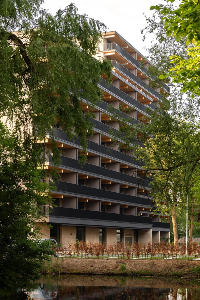 Tower facade with cantilevered balconies reflected in the canal at dusk through foliage