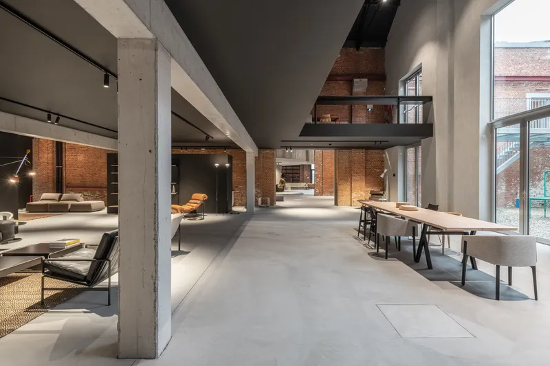 Double-height interior with concrete beams, exposed brick walls, and mezzanine overlooking dining area