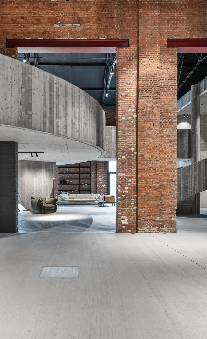 Curved concrete wall wrapping around brick columns under mezzanine with steel beams overhead