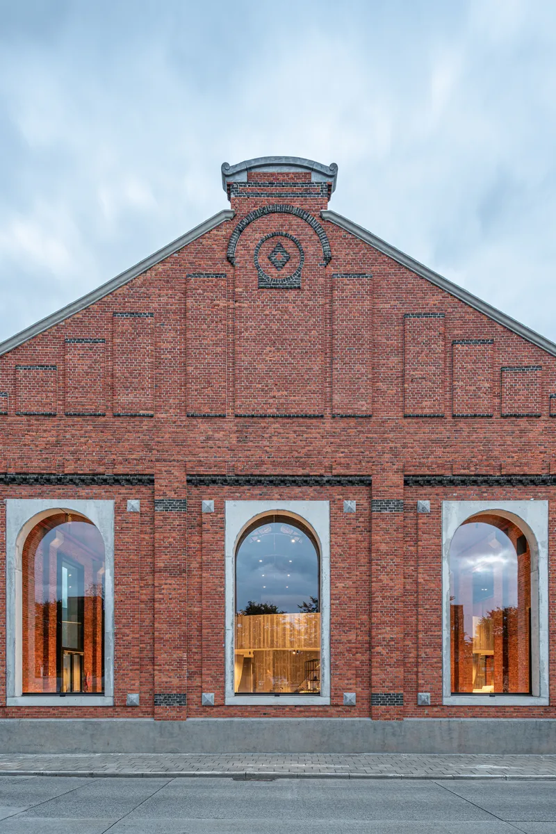 Frontal elevation showing the gabled brick facade with decorative medallion and three arched openings at twilight