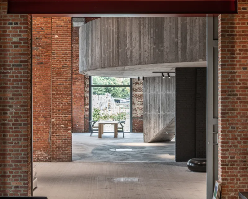 Interior view through exposed brick walls toward a cantilevered concrete volume and courtyard beyond