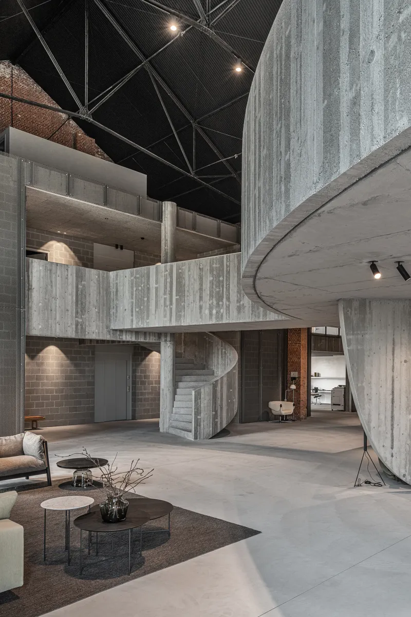 Double-height interior space with board-formed concrete stair and curved mezzanine under black metal ceiling
