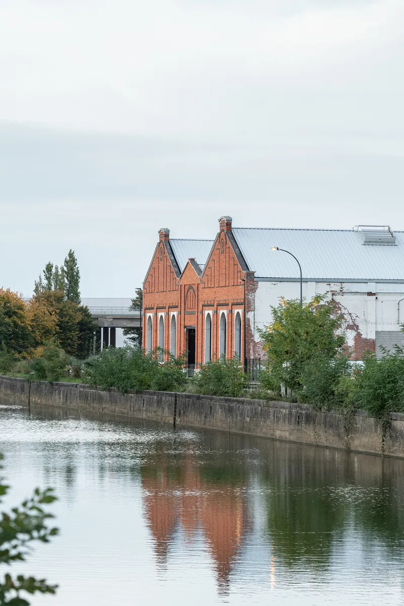 Red brick gable facade with twin chimneys reflected in the still canal water