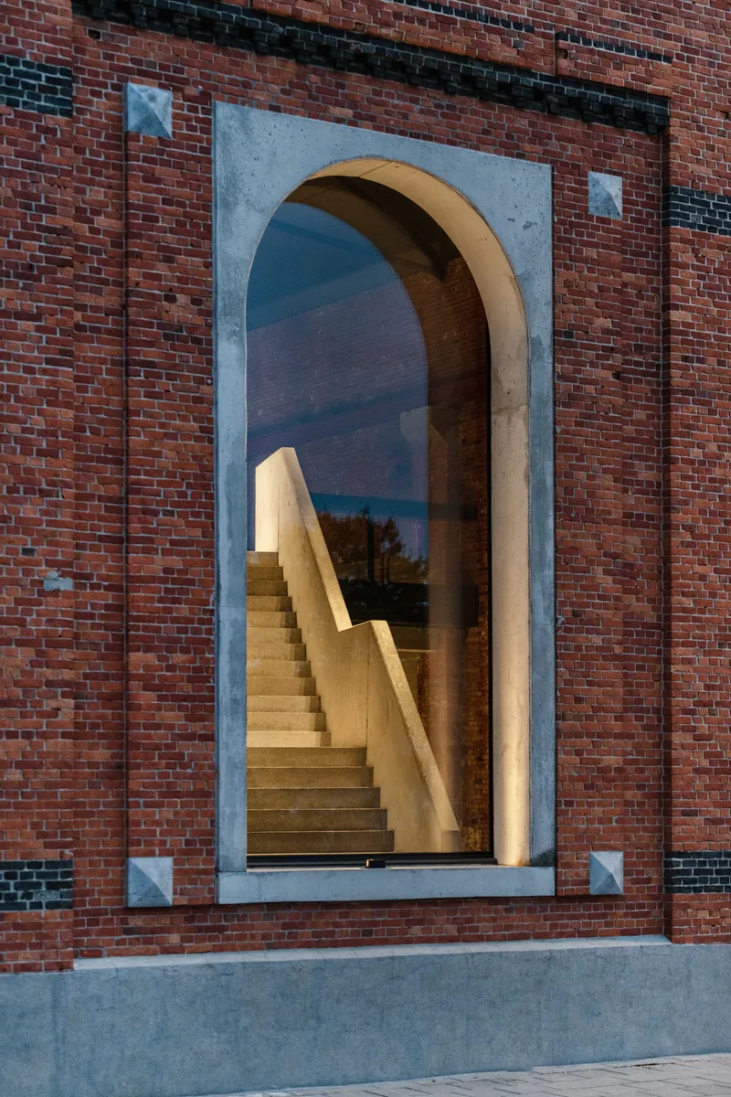 Arched window with pale concrete surround frames timber staircase behind glazing