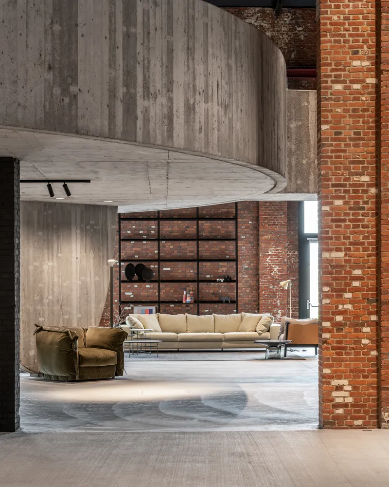 Double-height interior with curved concrete walls and exposed brick next to furnished seating area