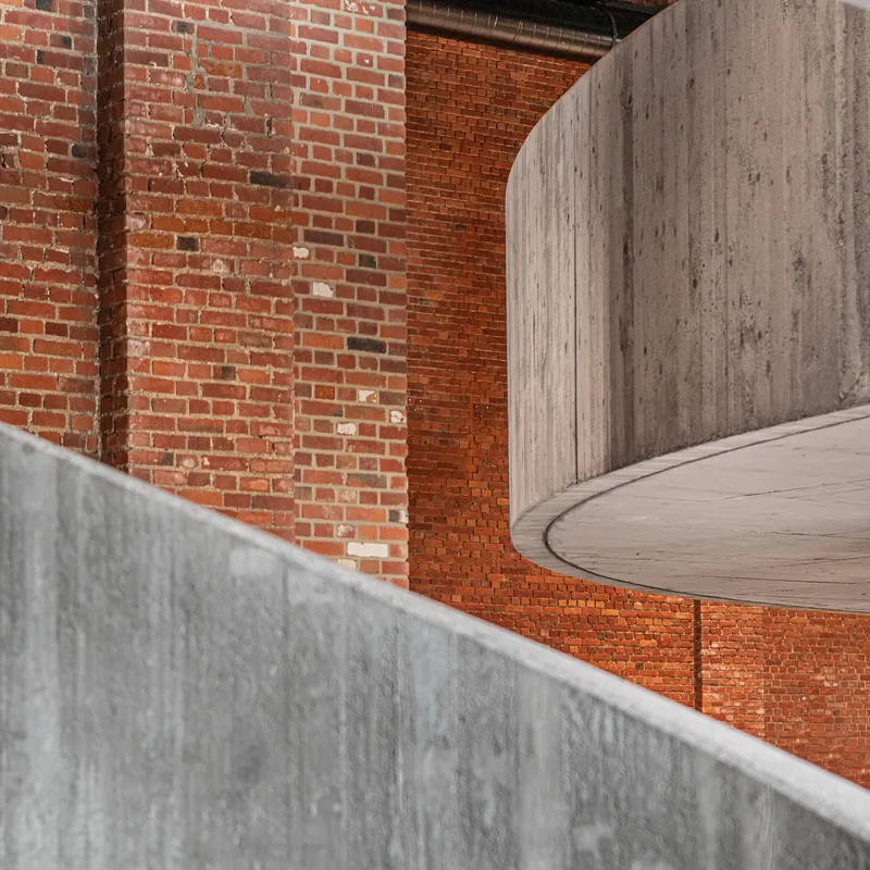 Detail of board-formed concrete curves meeting exposed brick wall with formwork texture