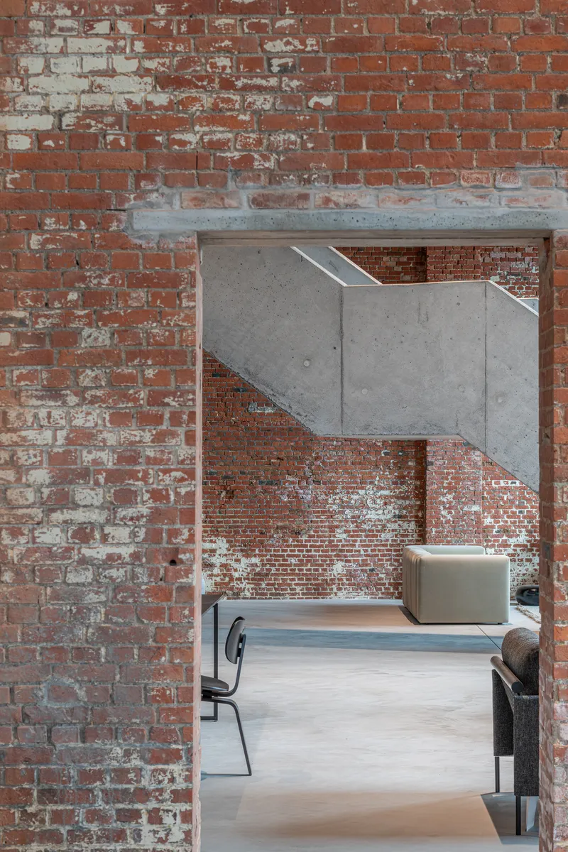 Exposed brick doorway framed by a cantilevered concrete beam above a seating area