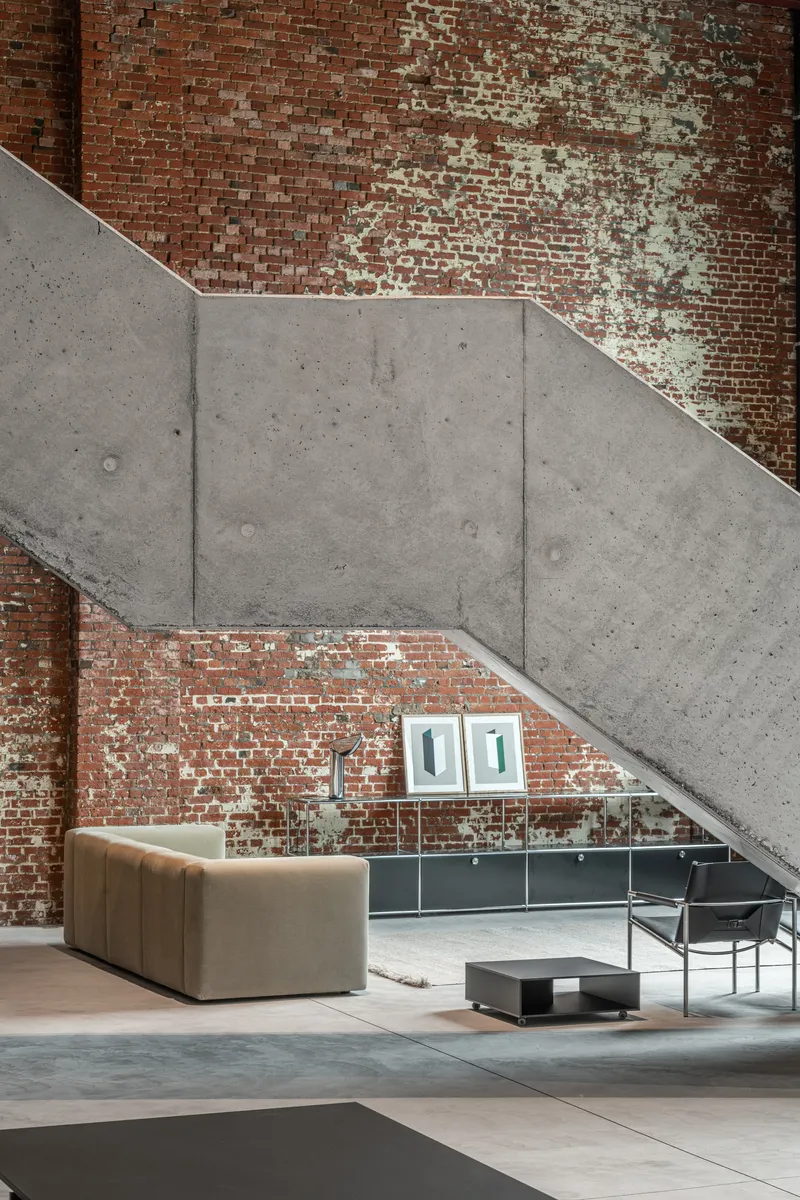 Angular concrete stair soffit cutting across weathered red brick wall with seating below
