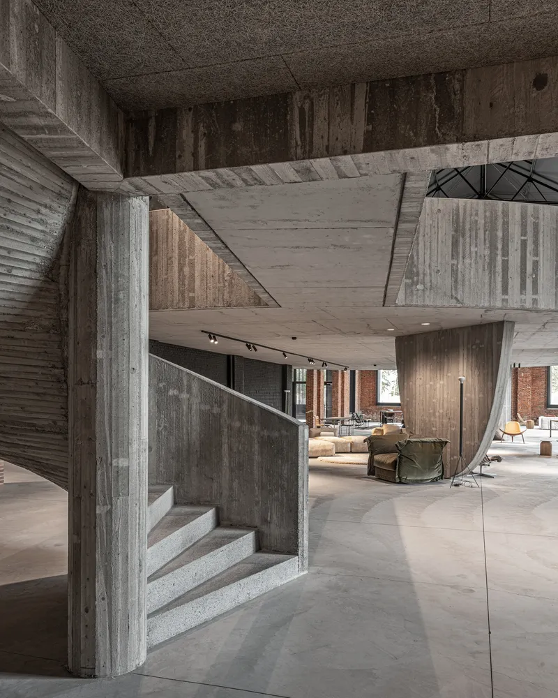 Concrete staircase wrapping around angular column beneath cantilevered upper floor slabs