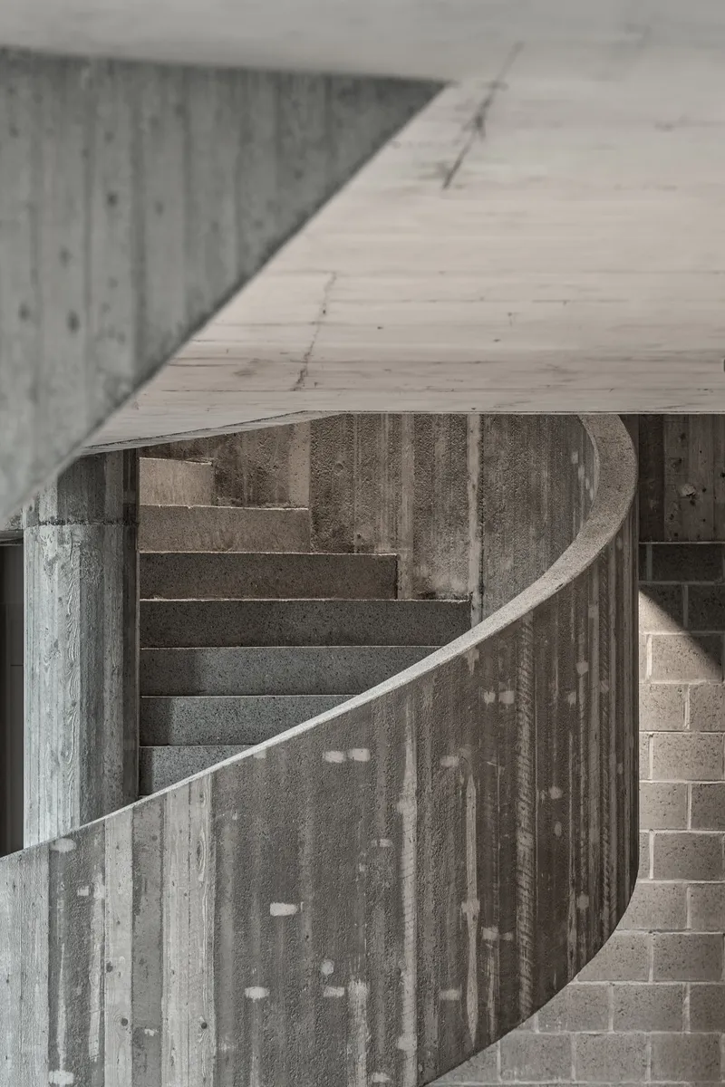 Curved concrete stair rail detail showing formwork texture and soffit edge in soft light
