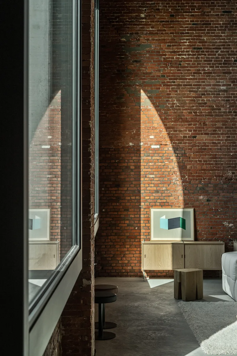 Interior view of exposed brick wall with tall window and triangular patch of afternoon sunlight