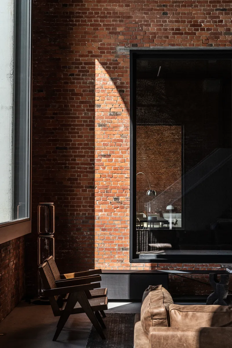 Exposed brick wall with black steel framed opening and triangular shaft of natural light