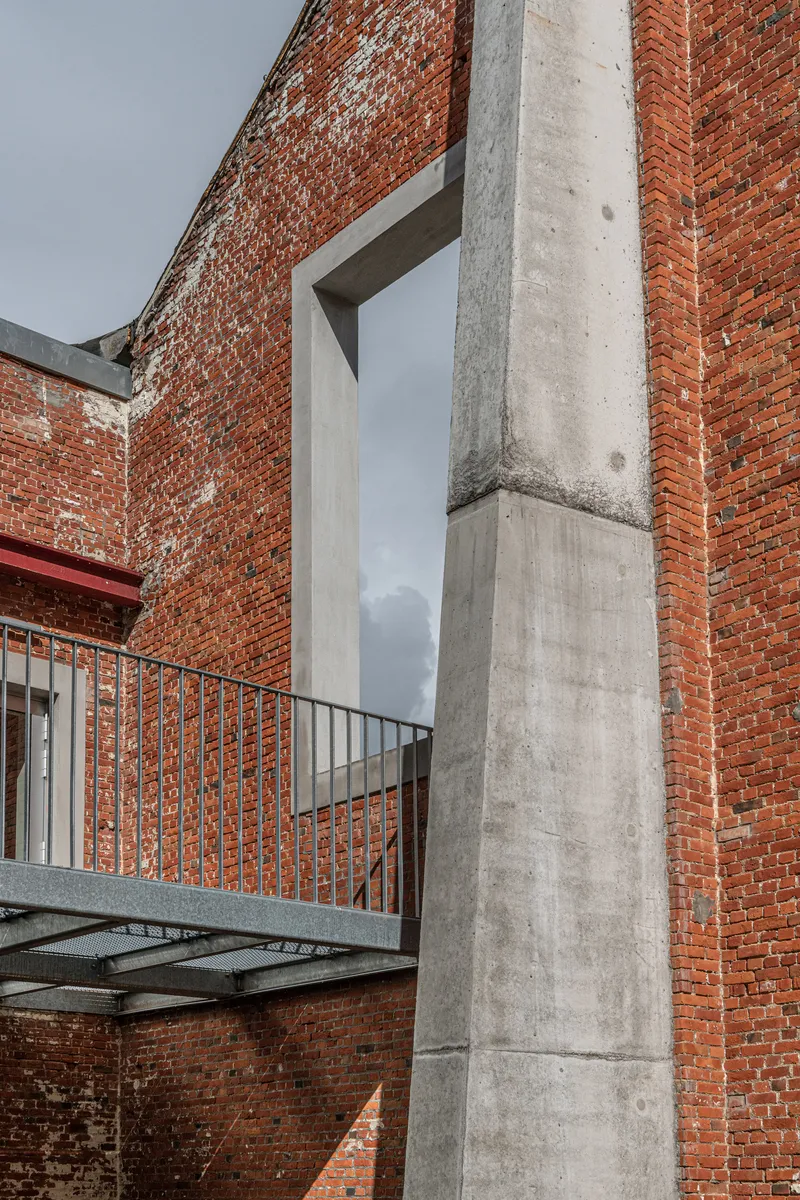 Concrete column and steel footbridge against weathered brick wall under overcast sky