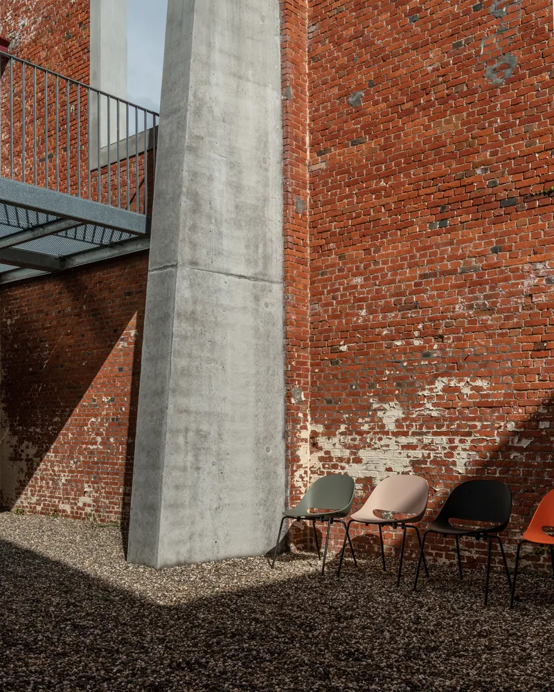 Concrete column base with three chairs on gravel courtyard beneath steel walkway