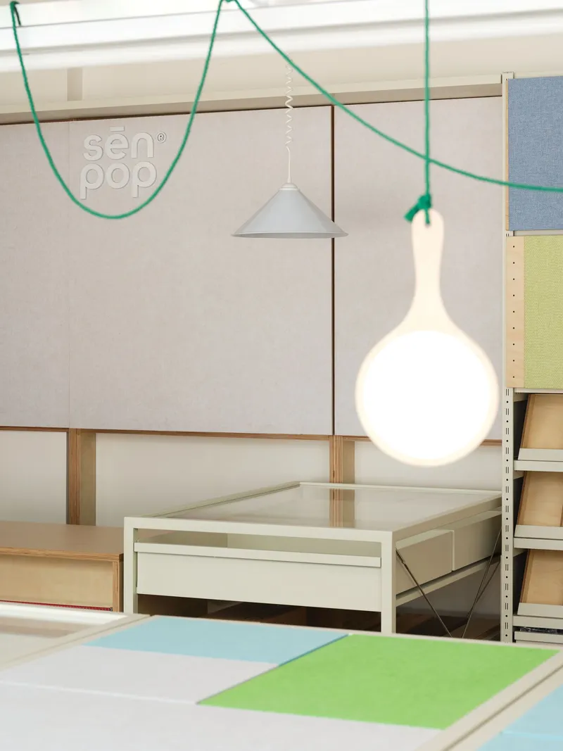 Close-up of white pendant lights hanging from green cables above plywood display tables with colored panels
