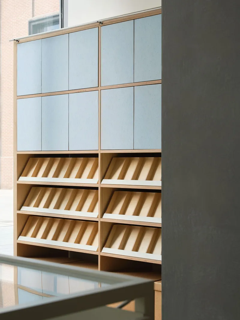 Angled shelving unit with pale blue cabinet doors and sloped display trays beside a grey steel column