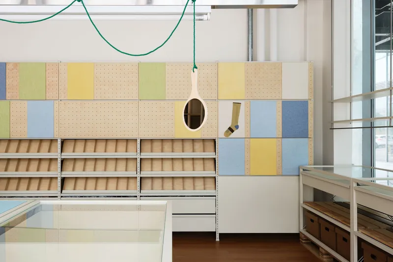 Modular storage wall with pastel pegboard panels, timber shelving units and pendant lights on green cables