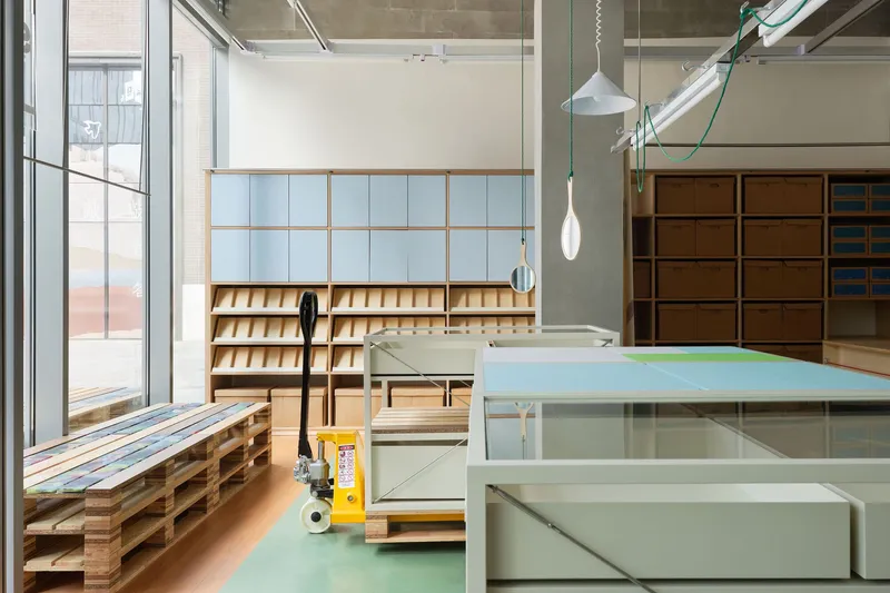 Workshop interior with movable tables on green flooring, timber shelving and exposed industrial ceiling