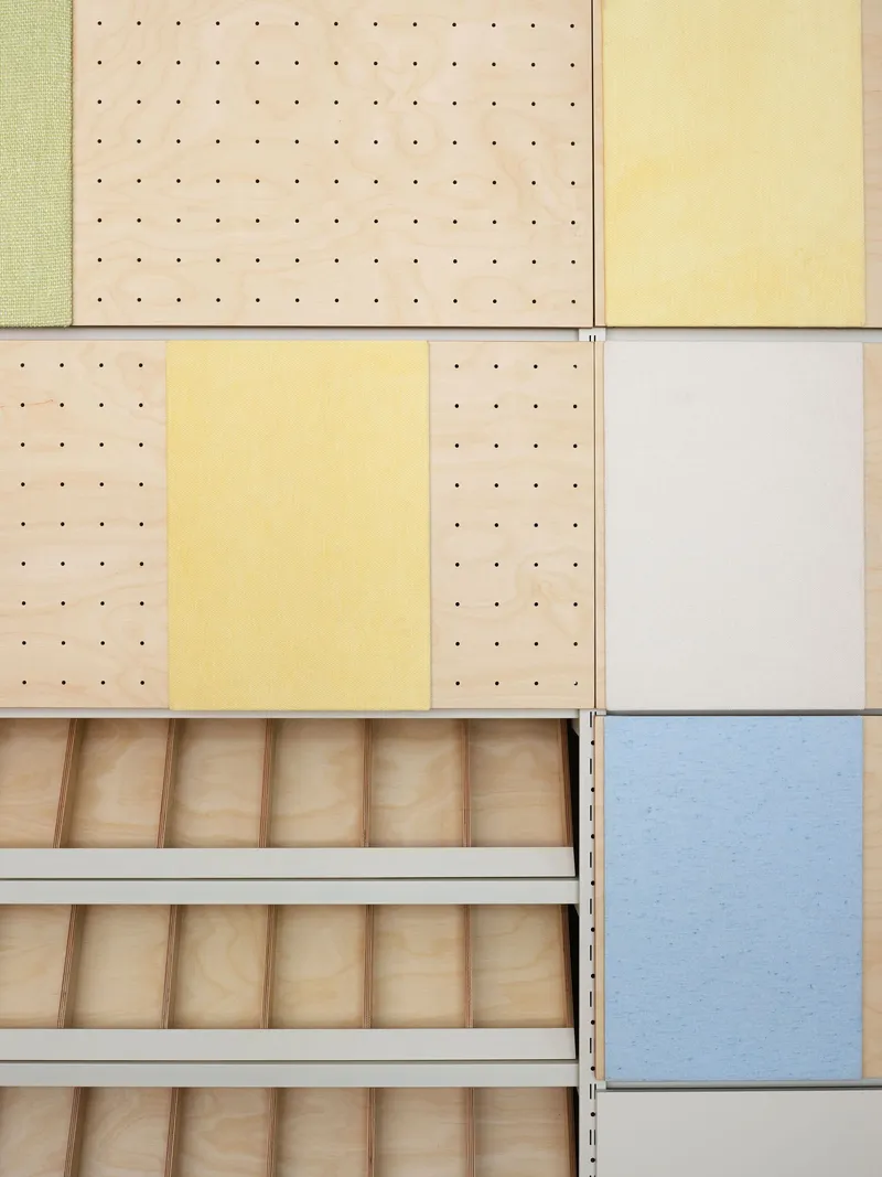 Material sample wall showing perforated plywood panels in pastel tones alongside open wooden drawer inserts