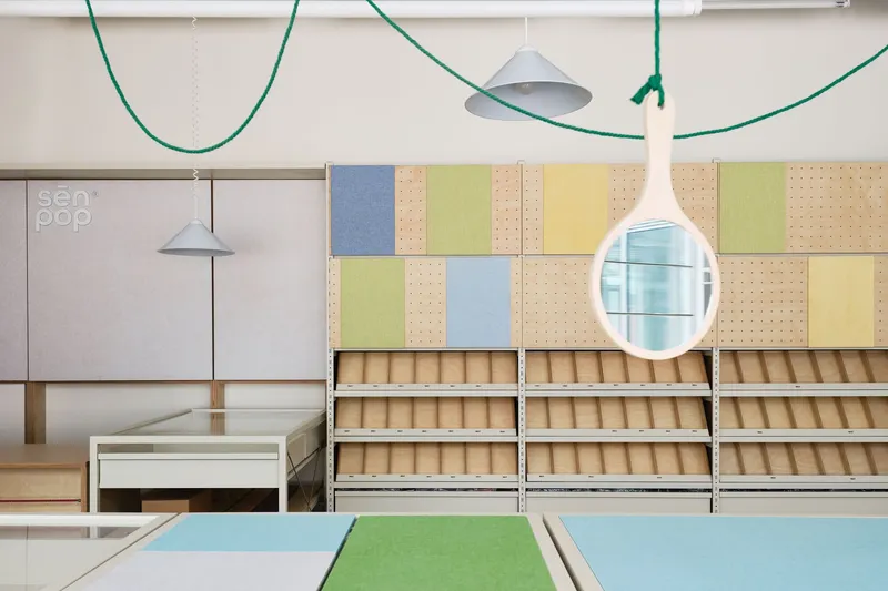 Display wall with plywood shelving units and multicolored perforated panels beneath pendant lights and green cable