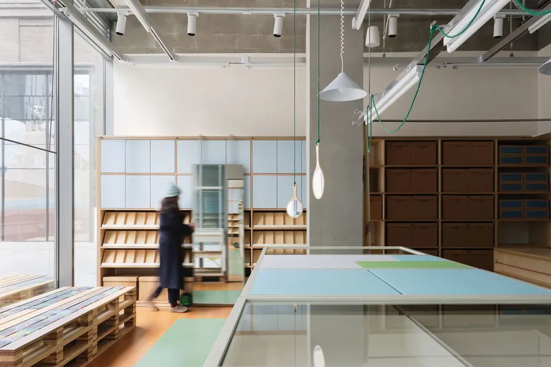 Interior retail space with exposed concrete ceiling and a person passing glass partitions near timber shelving